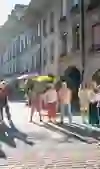 Eine Gruppe steht auf einer Kopfsteinpflasterstraße und lauscht einem Führer, der vor historischen Gebäuden in Bern steht. Sonnenlicht flutet die Szene und schafft eine lebendige Atmosphäre.