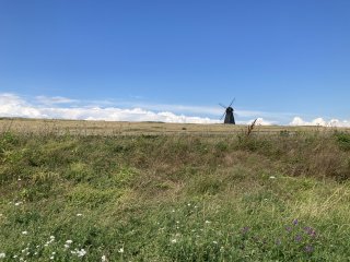 A black windmill stands in a grassy landscape under a clear blue sky.