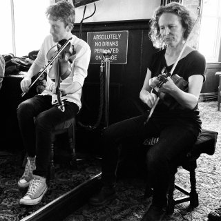 Two fiddlers side by side in a pub.