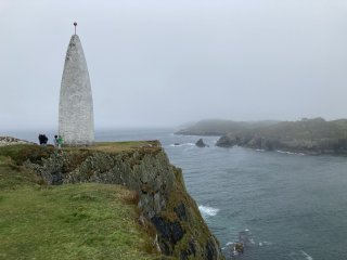 Looking past a white tapered tower on a cliff top to the ocean beyond.