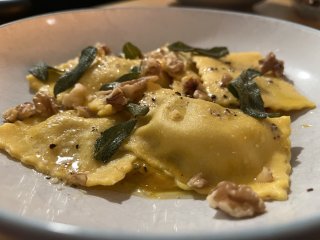 A dish of cooked ravioli garnished with sage and walnuts.