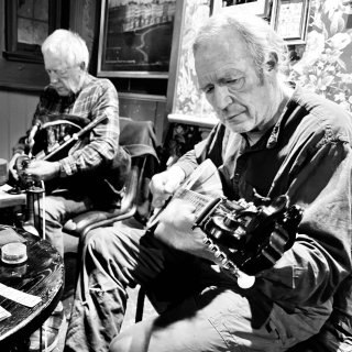 A man playing bouzouki accompanying a man playing the uilleann pipes in a pub.