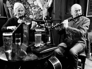 A woman playing fiddle and a man playing flute at a round pub table.