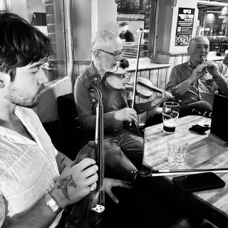 A fiddler listens as another fiddler plays with a whistle player.