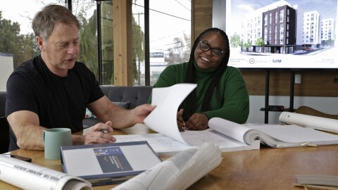 A photo of two people sitting at a desk reviewing blueprints. 