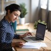 A woman wearing a polka-dotted blouse studies at her desk with her laptop and notes in front of her.