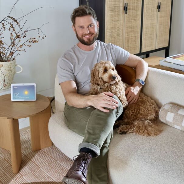 Bobby Berk sitting in a living room with a dog, decorative branches, and an Amazon Echo device