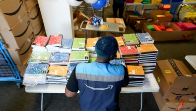 An Amazon employee stands in front of a table covered with composition and other school supplies. 