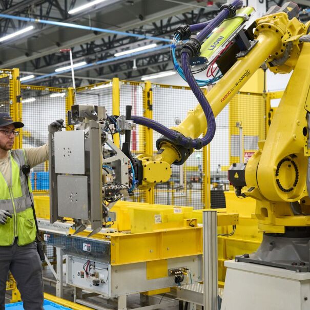 An Amazon employee in safety vest interacting with robotic equipment at a robotics facility