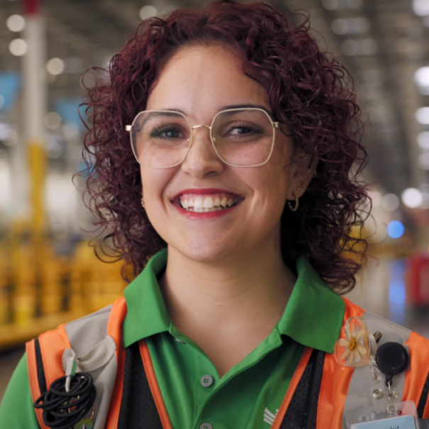 Smiling Amazon employee with curly hair and glasses wearing a safety vest