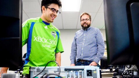 A teacher and a teacher observing a computer that is open and laid on a desk top.