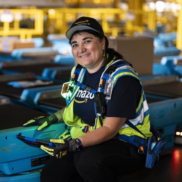 Woman in hat and safety vest posing with blue robotic equipment in Amazon facility.