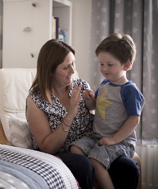 Hugo, in remission from leukaemia, propped on her knee and looking towards a grouping of cuddly toys.