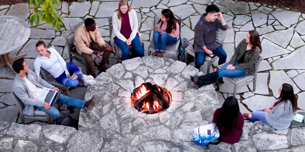 Overhead view of students sitting around an outdoor fire pit and talking.