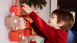 Little boy taking down a gift from an advent calendar hanging on the wall.