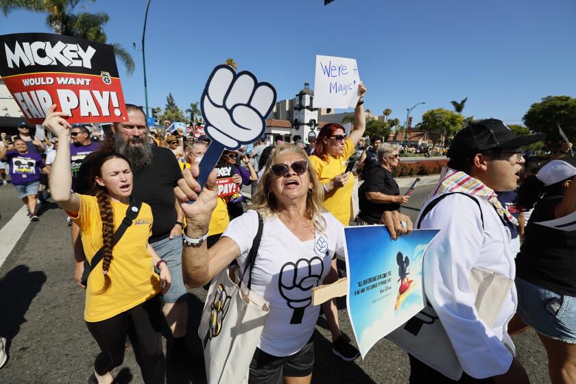 A group of workers marching down a street while shouting and holding picket signs during a demonstration.