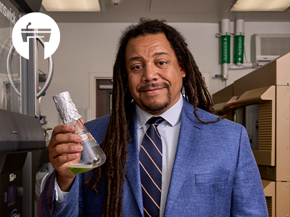 Image of Bil Clemons in blue suit and tie holding a beaker with green liquid