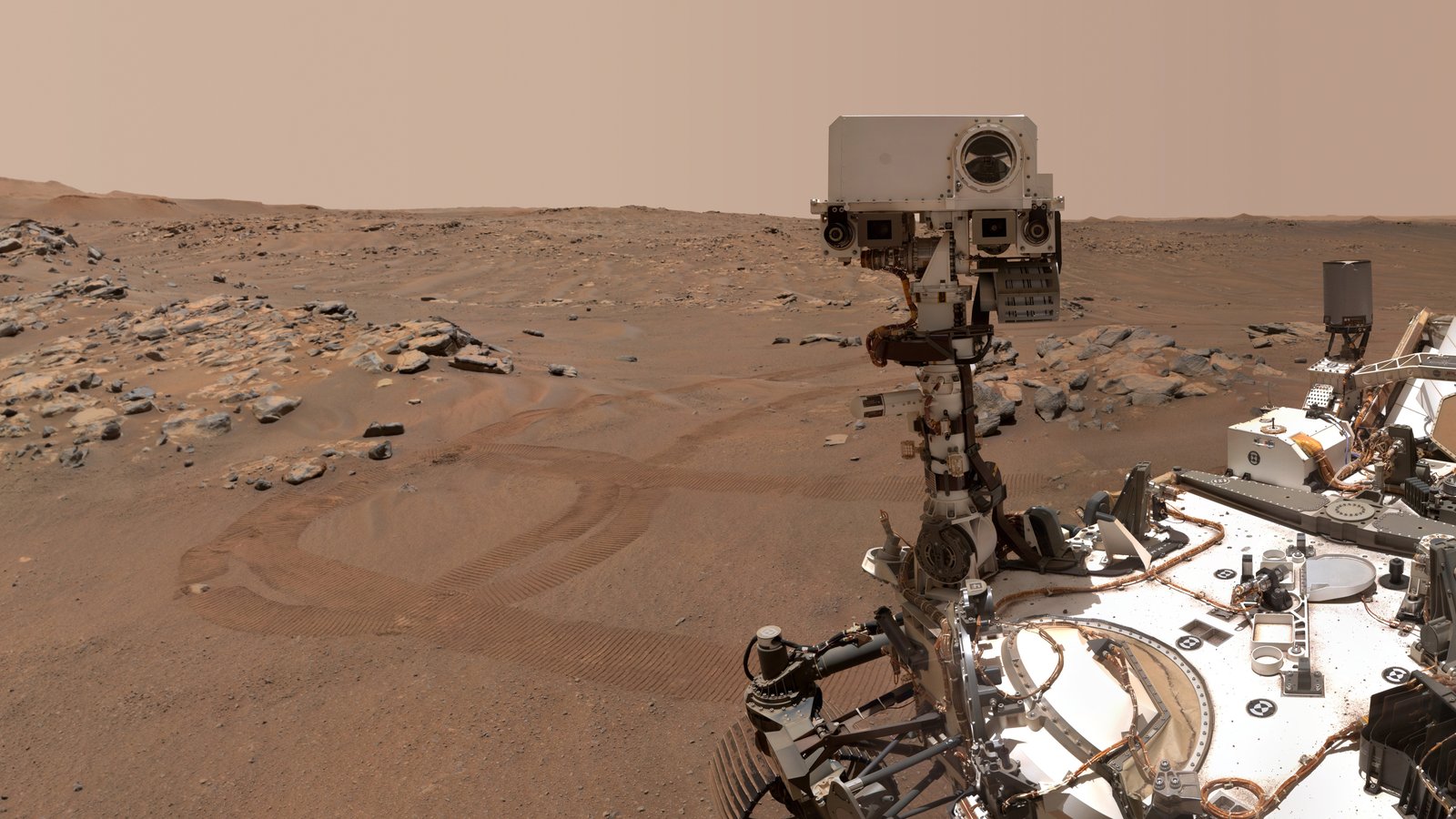 An image of the Mars Perseverance rover against a red-brown Martian landscape