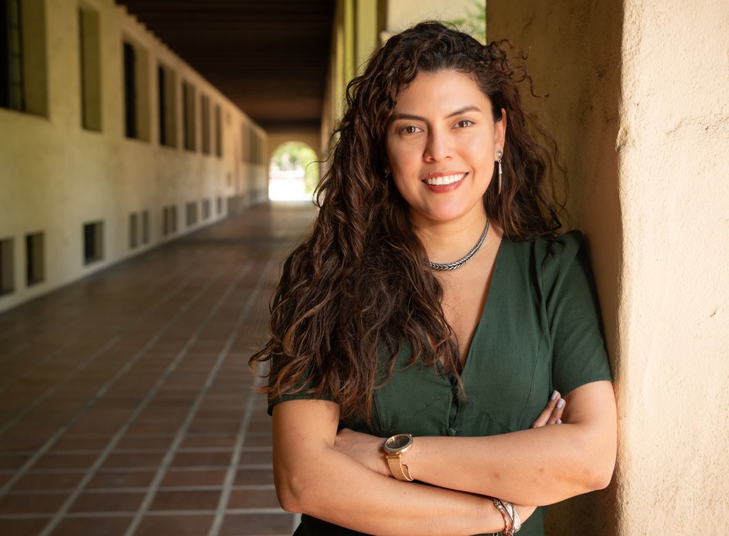 A woman in a green dress stands outside at the Caltech campus for a photo