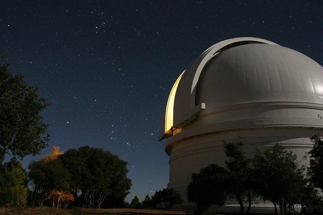 Exterior view of Palomar Observatory with night sky full of stars in background.