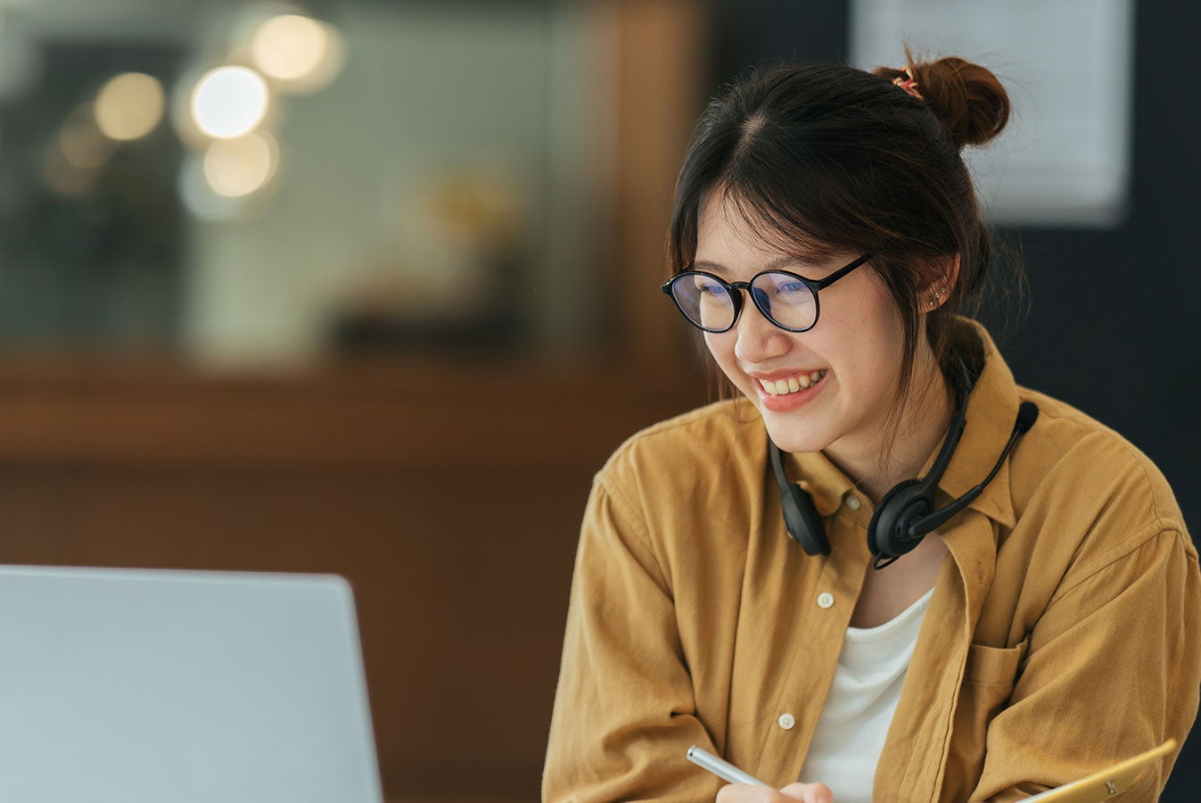 Smiling woman sitting and looking at laptop with a pen in hand.