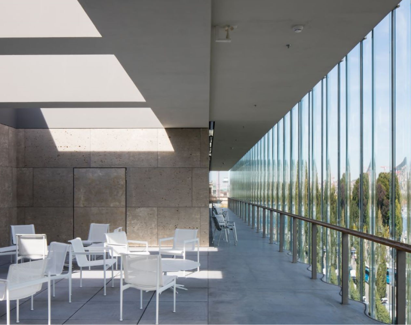 Modern outdoor terrace with white chairs and tables, featuring large glass windows and geometric shadows