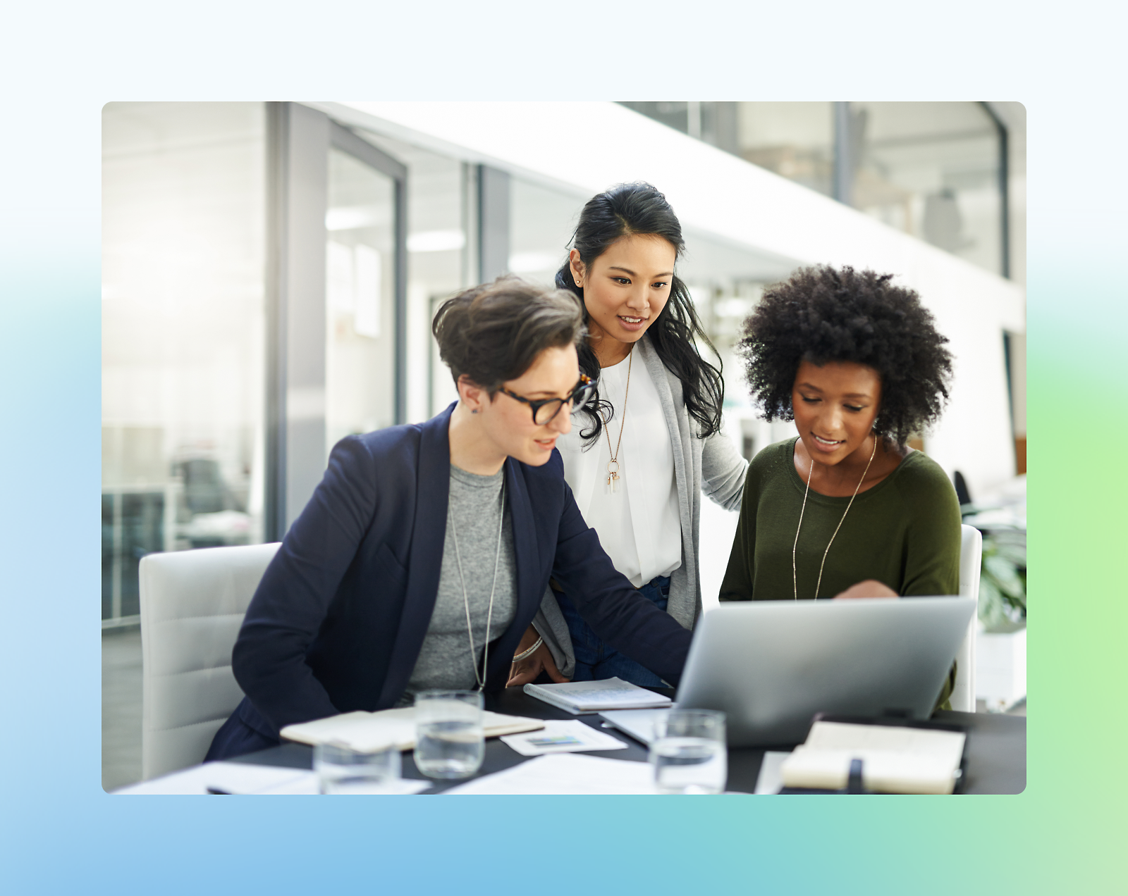 Three diverse women collaborating at a laptop in a modern office setting.