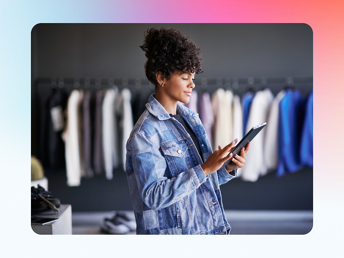 A woman in a denim jacket is using a tablet in a clothing store