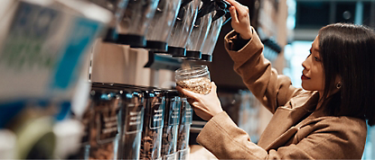 A woman picking up a jar in a grocery store.