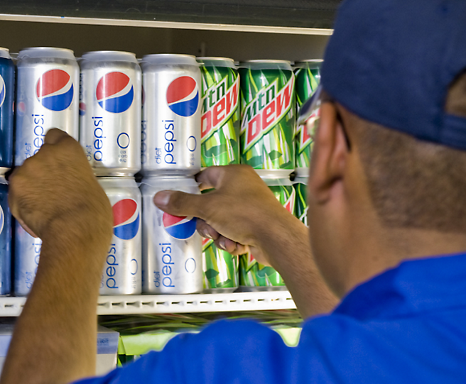 A man in a blue shirt picking up a can of pepsi.