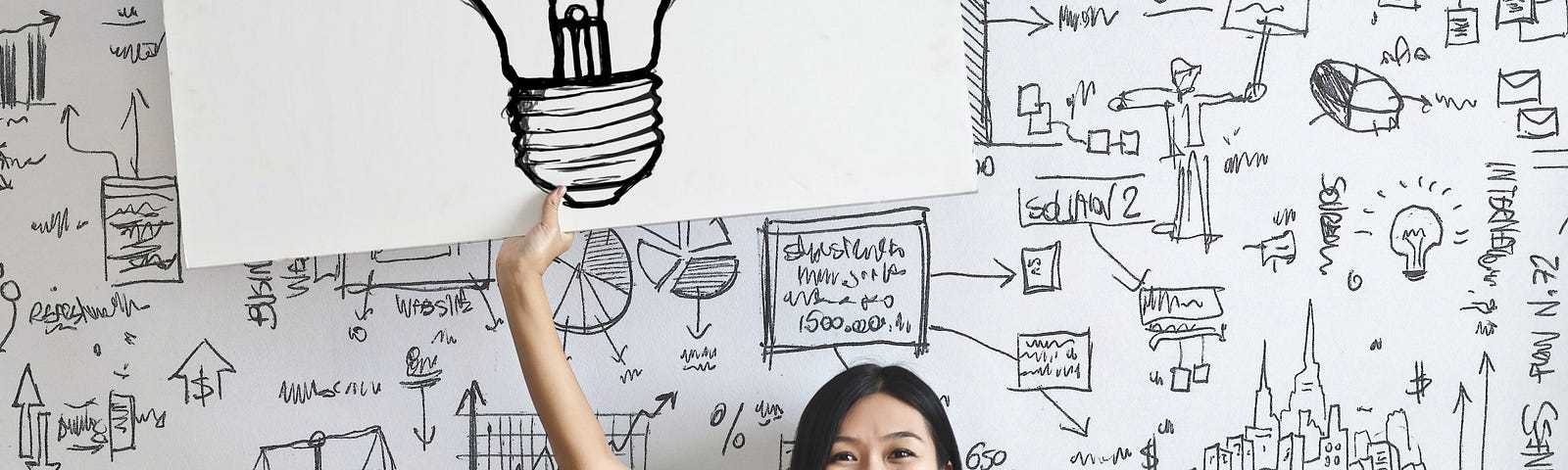 Young Asian woman sitting cross-legged on the floor and holding up a large poster picture of a light bulb.