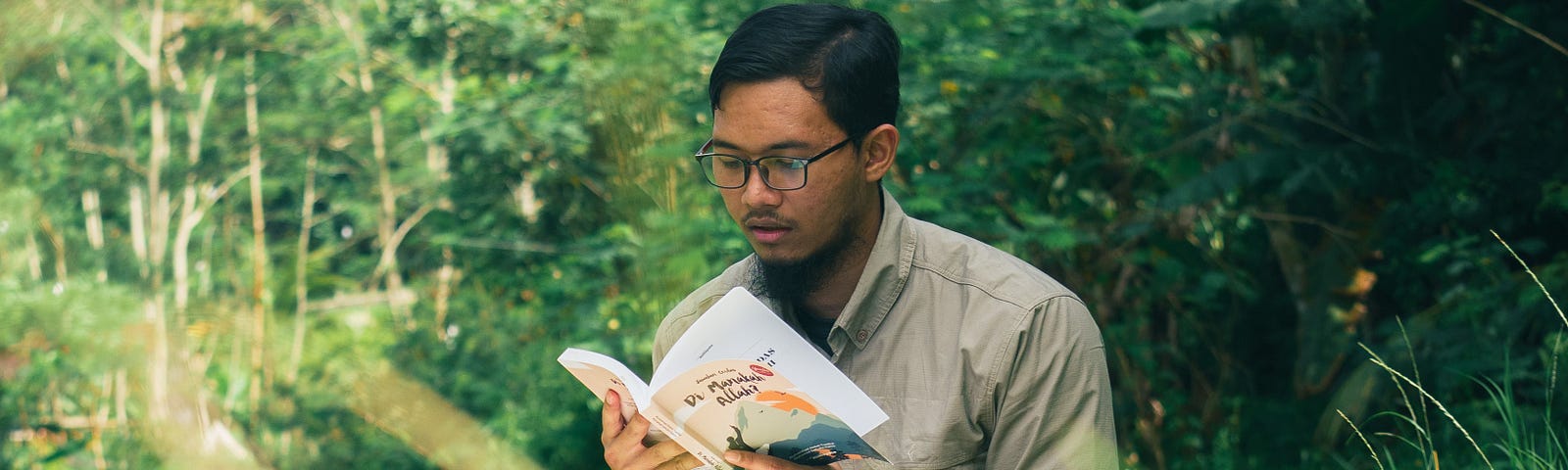 Young man reading book near river.