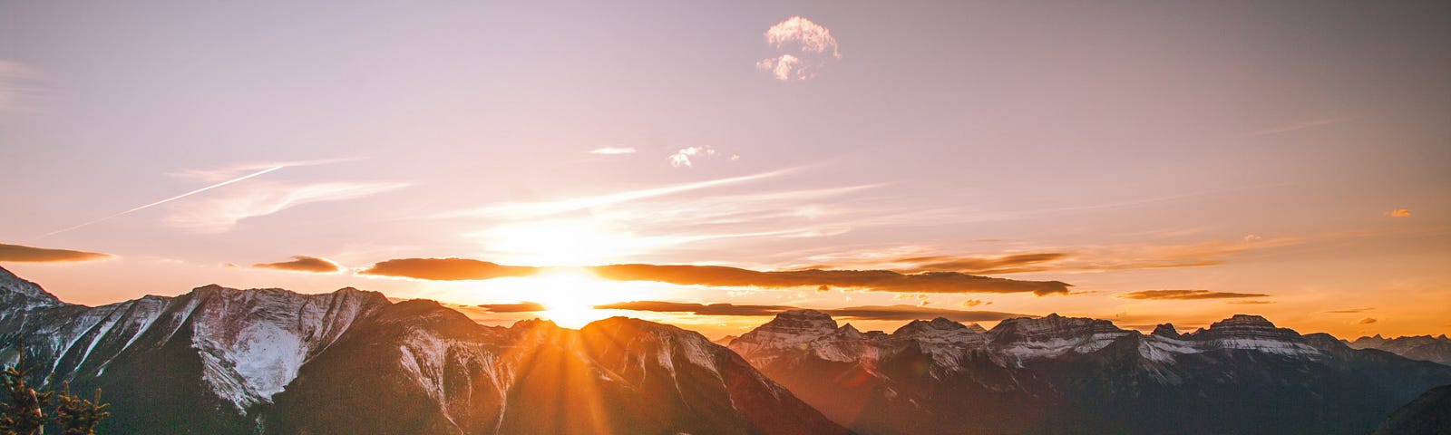 The sun setting behind a mountain range with snowy peaks