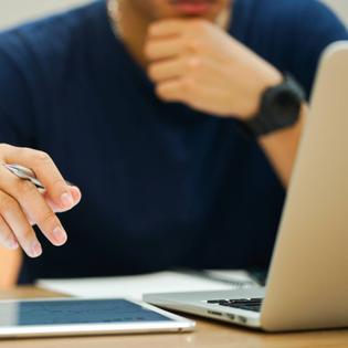 Close-up of a man on his Macbook holding a pen in his hand.