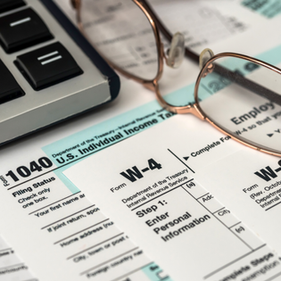 A pair of glasses and the edge of a keyboard are next to a W-4 and a 1040 form. 