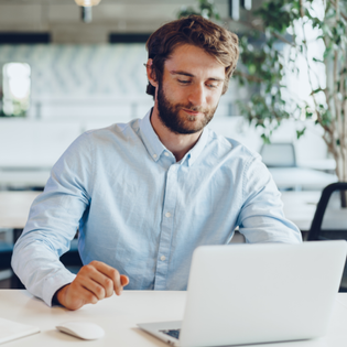 A man in an office stares down at his laptop. 