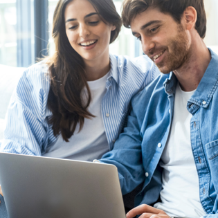 A man and woman sit on the couch while they use a laptop.