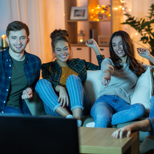 A group of friends sit on the couch while watching TV and laughing.