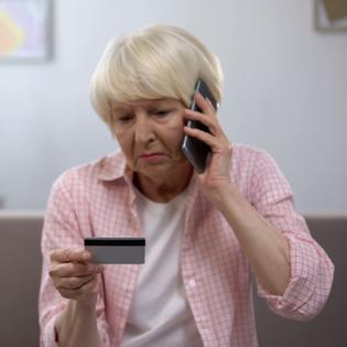 Senior lady looks upset on the phone as she looks at her credit card