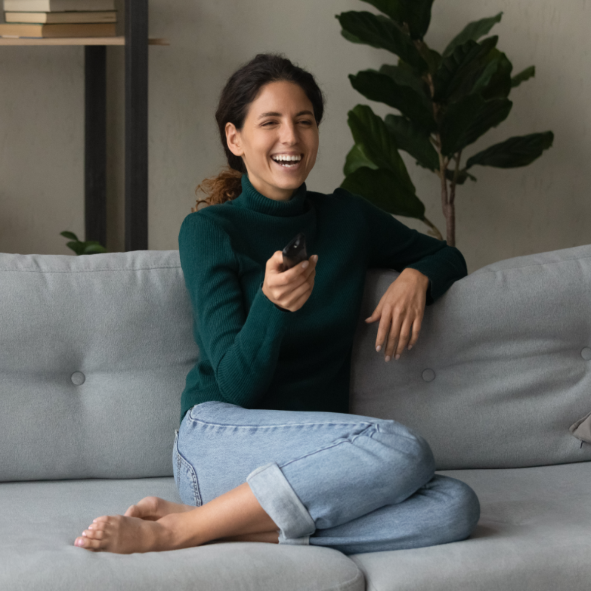 A woman holds a remote while laughing on the couch.