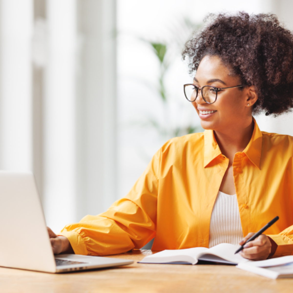 A woman scrolls on her laptop while taking notes.