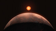 The image is an artist’s impression of an exoplanet. A rusty planet looms in the forefront, half of its sphere taking up most of the frame. The top of the planet is brown and red, illuminated by a small star shining in the distance. The lower part of the sphere is shrouded in darkness. The star is aligned with the planet, in the middle of the image. Compared to the giant planet, the star looks small. In the black background are some very tiny stars.