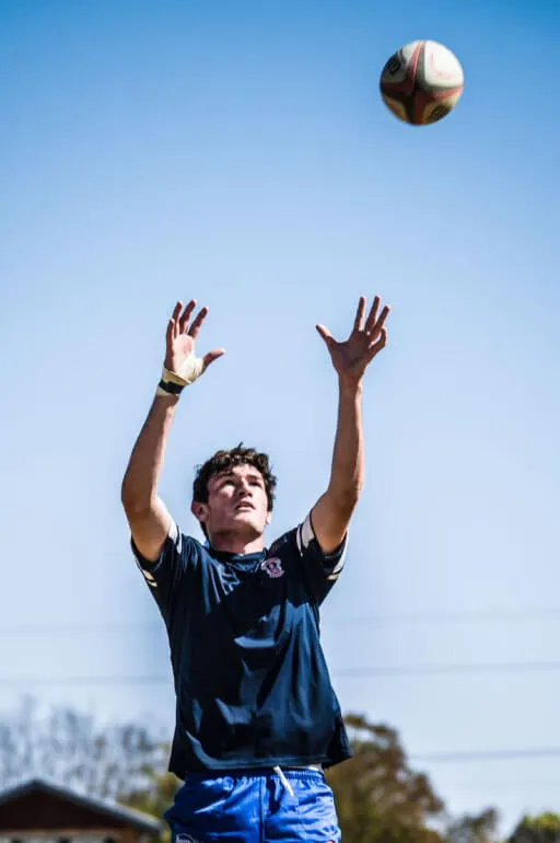 A boy jumps up in the air to catch a rugby ball.