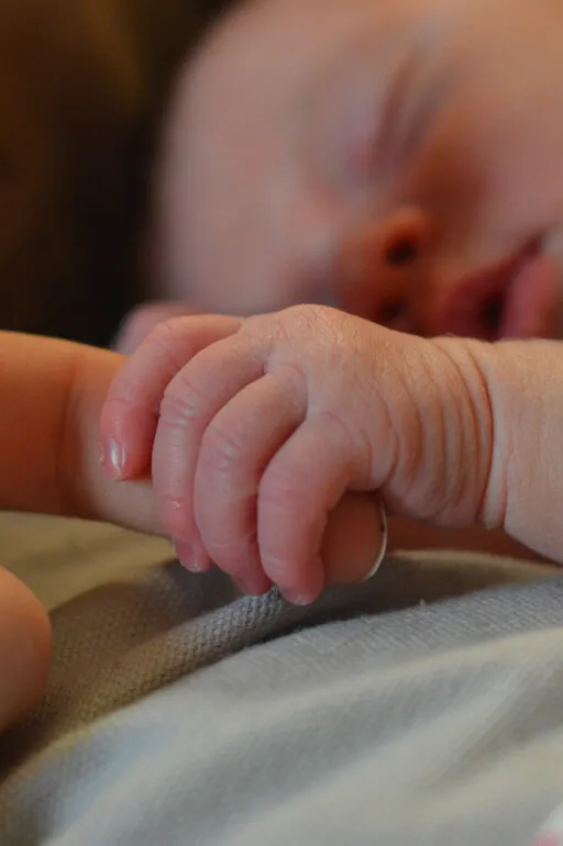 A baby's hand is holding a adult's finger.