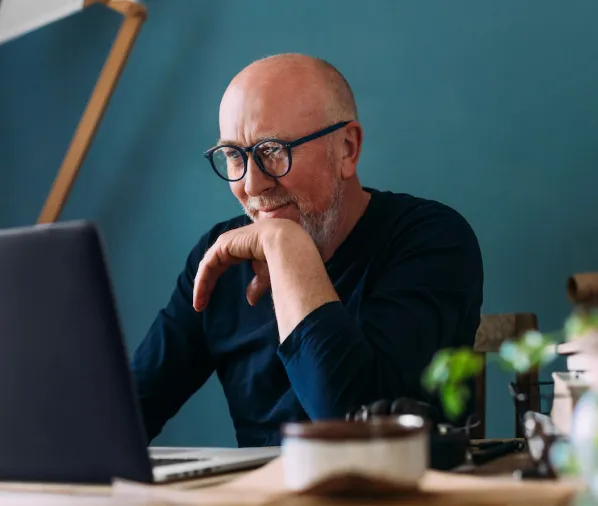 Guy with glasses smiling and looking at his laptop wearing a navy shirt