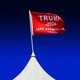 A color photograph of a white pointed tent top with a red "Trump 2024" flag on top