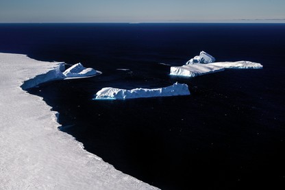 photo of curving white edge of glacier with several calved icebergs and dark blue sea