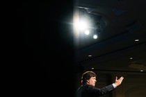 Tucker Carlson addresses an audience with a spotlight overhead.