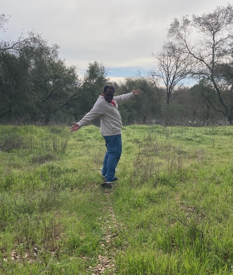 Me looking backwards as I gesture to the sky while walking on a small trail.