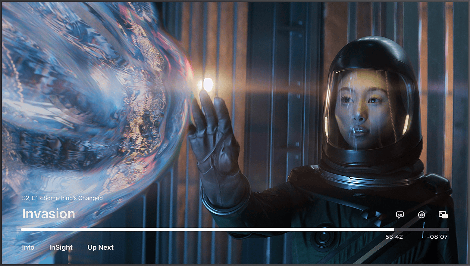 Apple TV 앱이 일시 정지되어 있고 제어 항목이 표시되어 있습니다. 에피소드는 Invasion의 'Something’s Changed'입니다. 오른쪽 하단의 진행 막대 위에 자막 언어 버튼과 오디오 버튼이 있습니다.